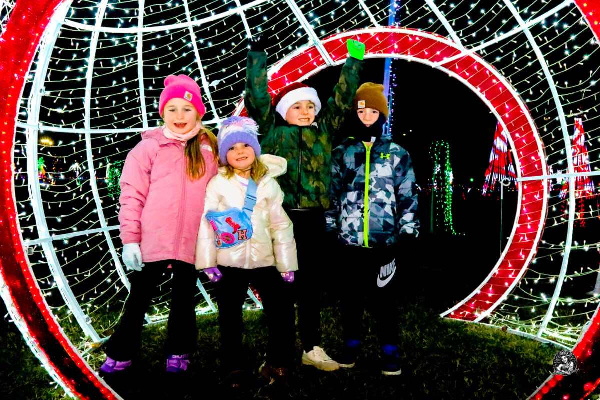 Four children under a lit archway on the Christmas light trail
